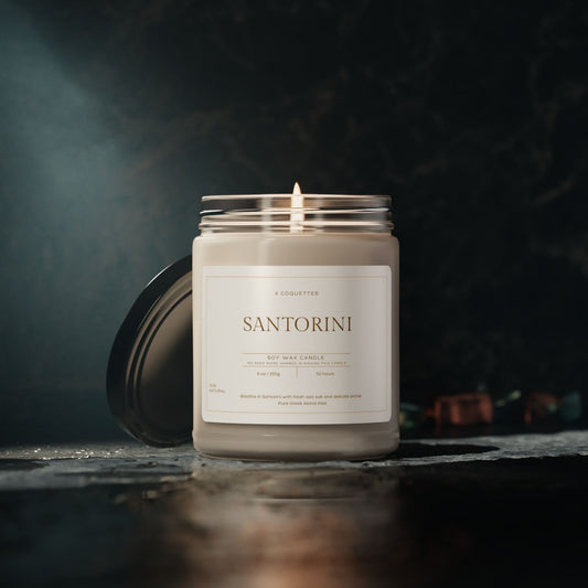 A lit Santorini scented candle labeled Greek Island Bliss rests on a polished surface. The eco-friendly candle jar is open with its lid placed beside it, while the dimly lit background adds a warm and cozy ambiance. Perfect for Martin Luther King Jr. Day 2025